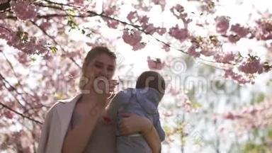 年轻的妈妈抱着她的小儿子，孩子在盛开的樱花树下，<strong>飘落</strong>的粉红色花瓣和